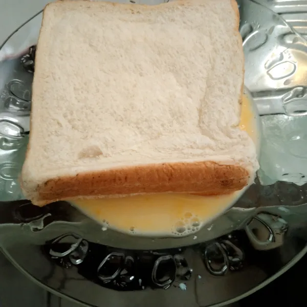 Baluri setiap sisi roti oleh kocokan telur dan susu.
