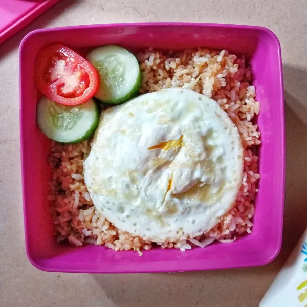 Tata nasi goreng dalam kotak bekal. Tambahkan telur ceplok, mentimun dan tomat sebagai pelengkap.