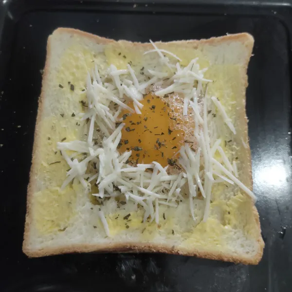 Tuang putih telur kedalam roti lalu masukkan kuning telur, beri taburan keju parut dan parsley kering.