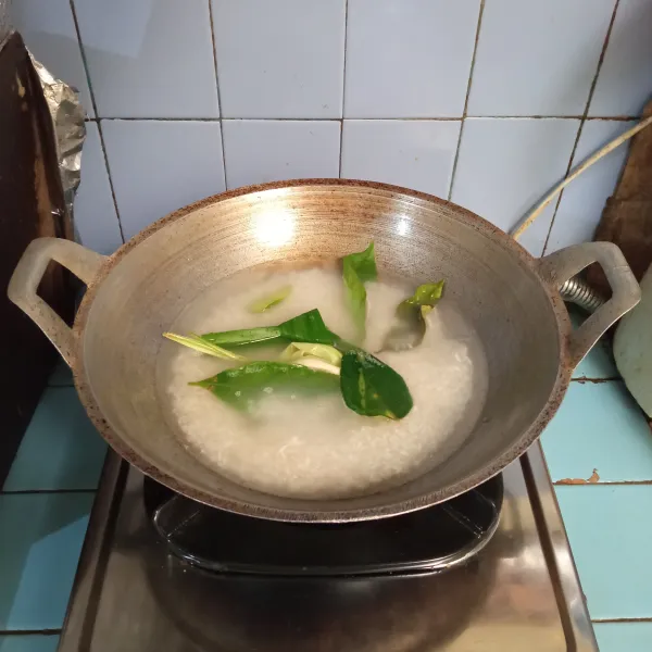 Masukkan beras ke dalam wajan, lalu tuang air, tambahkan daun salam, daun jeruk dan serai.