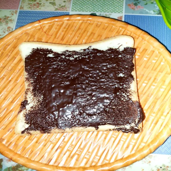 Siapkan roti tawar, kemudian olesi dengan selai coklat secukupnya.