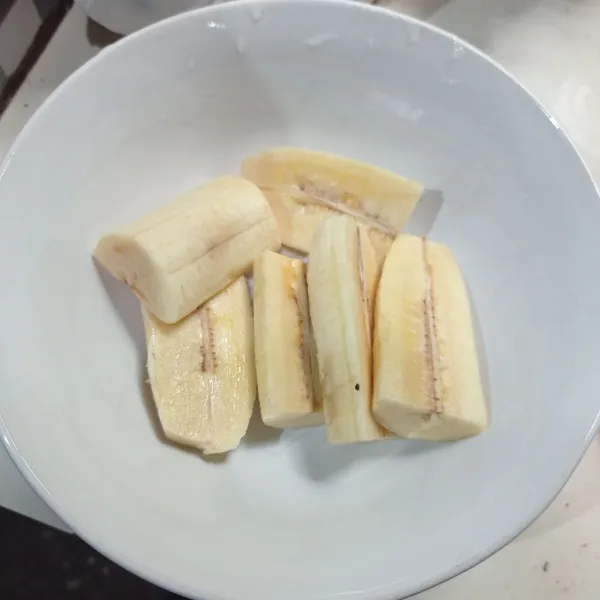 Kupas pisang, lalu potong jadi 3 bagian, tiap bagian belah jadi 2.