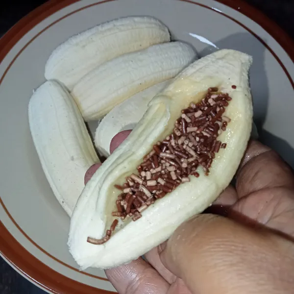 Kupas pisang dan belah tengahnya, lalu isi dengan cokelat meses secukupnya.