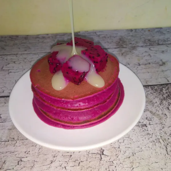 Sajikan pancake dengan potongan buah naga dan krimer kental manis.