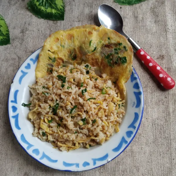 Taruh telur dadar di pinggir piring, kemudian tambahkan nasi goreng dan sajikan hangat.