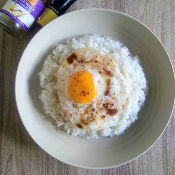 Letakkan telur di atas nasi. Kemudian tambahkan kecap asin, minyak wijen, dan sambal tabur.