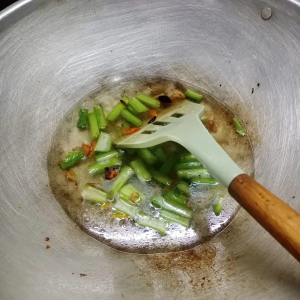 Masukkan batang sawi, aduk rata. Tuang air, masak sampai batang sawi setengah matang.