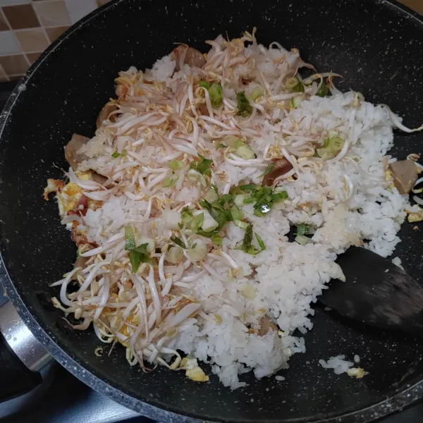 Tambahkan nasi putih, tauge dan irisan daun bawang. Aduk rata.