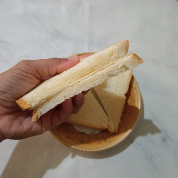 Ambil satu roti beri isian keju slice, lalu tutup kembali dengan roti.