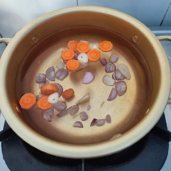 Siapkan 700 ml air dalam panci. Tambahkan irisan bawang putih, bawang merah dan wortel. Rebus hingga wortel empuk.