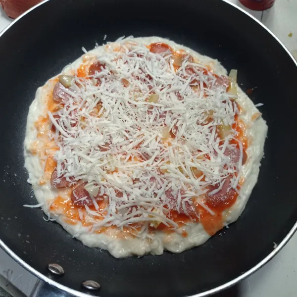 Olesi adonan pizza dengan saus sambal dan saus tomat, ratakan lalu beri tumisan sosis, terakhir taburi keju cheddar parut.