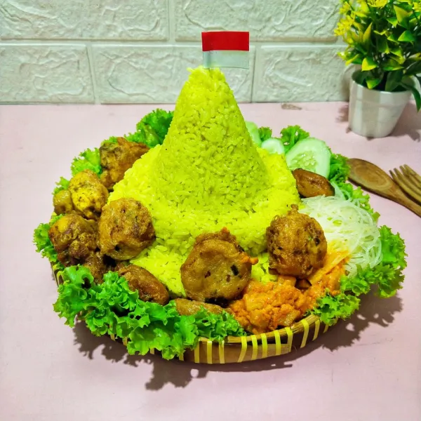 Kemudian hias nasi kuning tumpeng dengan lauk pauk lainnya dan beri hiasan bendera merah putih lalu siap disajikan.