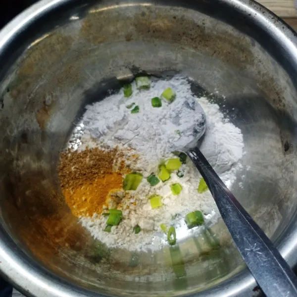 Dalam wadah masukkan tepung terigu, tepung beras, daun bawang, bawang putih bubuk, ketumbar bubuk, kunyit bubuk, kaldu bubuk, dan garam.