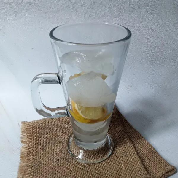 Masukkan es batu dan potongan lemon ke dalam gelas.