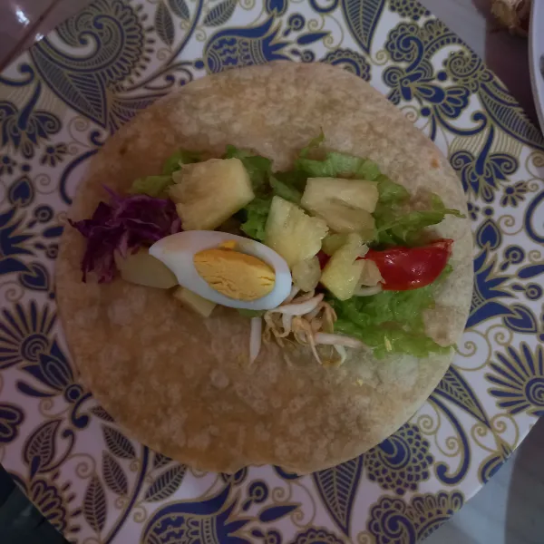 Panggang tortilla di pan anti lengket, lalu bolak-balik hingga muncul kecokelatan. Kemudian angkat dan taruh potongan sayur, buah, serta telur rebus di atas tortilla.