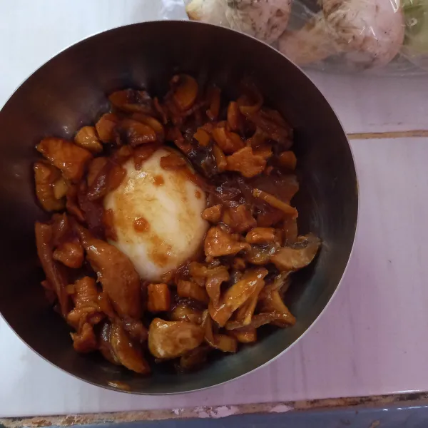 Siapkan mangkuk, taruh setengah butir telur rebus, lalu tuang tumis ayam.