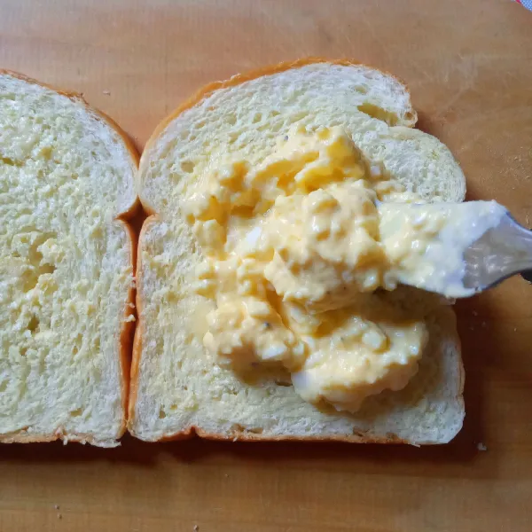Siapkan roti tawar. Oles masing-masing lembar roti dengan setengah sendok teh mentega tawar. Beri setengan bagian salad telur di salah satu rotinya, ratakan.