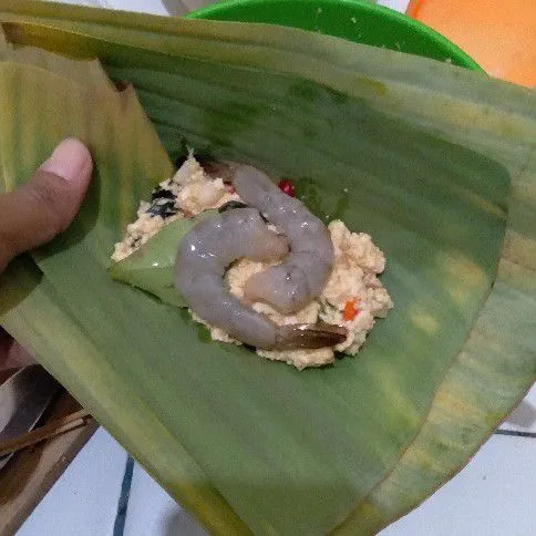 Taruh secukupnya tahu pada daun pisang. Pada bagian atas tambahkan daun salam dan udang, lalu bungkus.