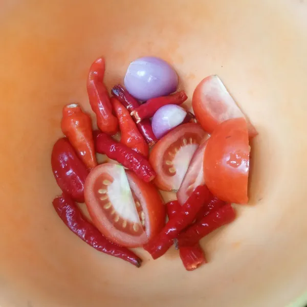 Potong-potong tomat dan cabai merah keriting, buang tangkai cabai rawit dan kupas bawang merah.