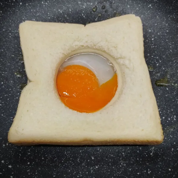 Pecahkan telur di dalam lubang roti tawar. 
Beri sejumput garam.