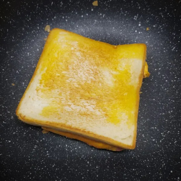 Tutup dengan roti tawar. Balik lagi perlahan kornet telur. Beri roti tawar lagi di atasnya. Panggang bolak balik roti tawar sampai sedikit kecoklatan.