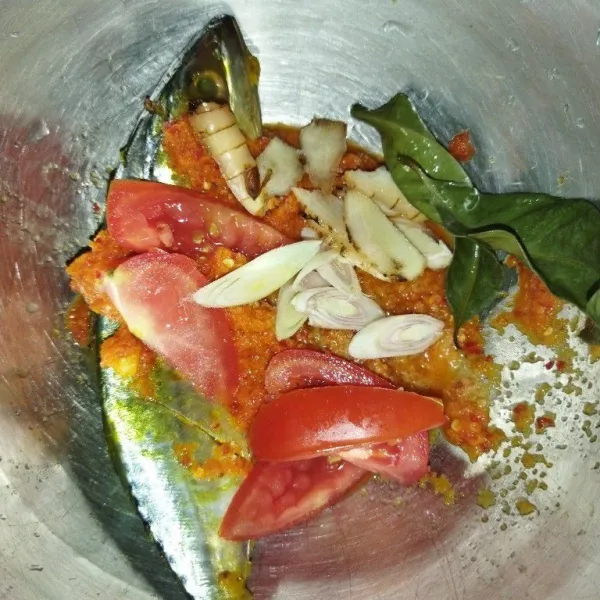 Siapkan ikan kembung yang sudah dibersihkan, lalu masukkan bumbu halus, daun salam, potongan serai, lengkuas dan tomat.