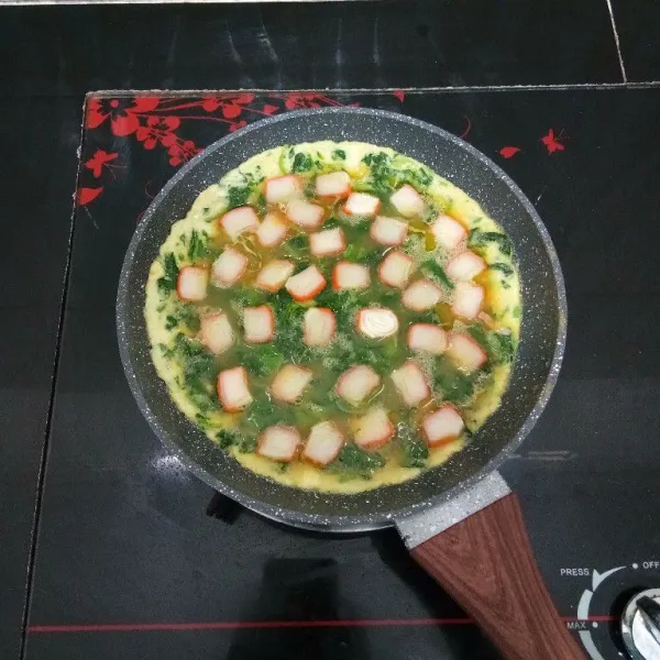 Lalu tata potongan crab stik di atasnya, lanjutkan memasak hingga kedua sisi omelette matang. Kemudian angkat.