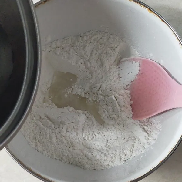 Masukkan tepung ketan, lalu beri garam. Kemudian tambahkan sedikit demi sedikit air panas.