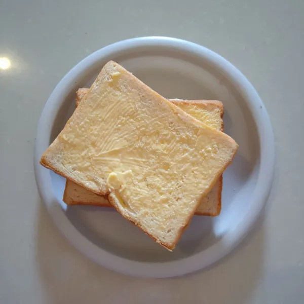 Beri margarin merata ke permukaan roti.