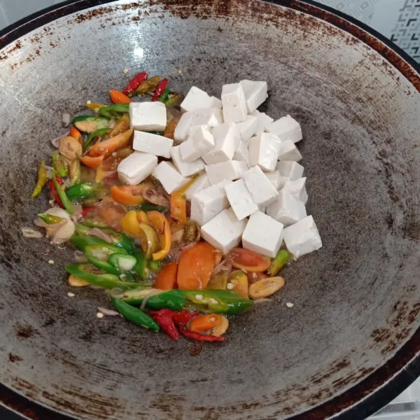Tumis bawang putih lalu bawang merah hingga wangi, kemudian masukkan cabe dan tomat, aduk rata. Lalu masukkan potongan tahu, aduk rata kembali, beri sedikit air.