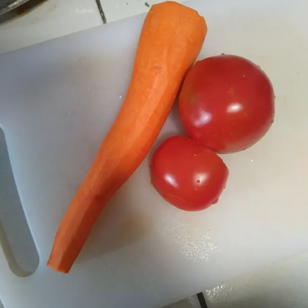 Kupas kulit wortel lalu cuci bersama tomat hingga bersih.