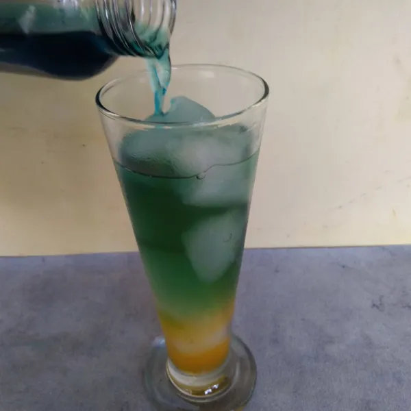 Tambahkan air soda biru ke dalam gelas.