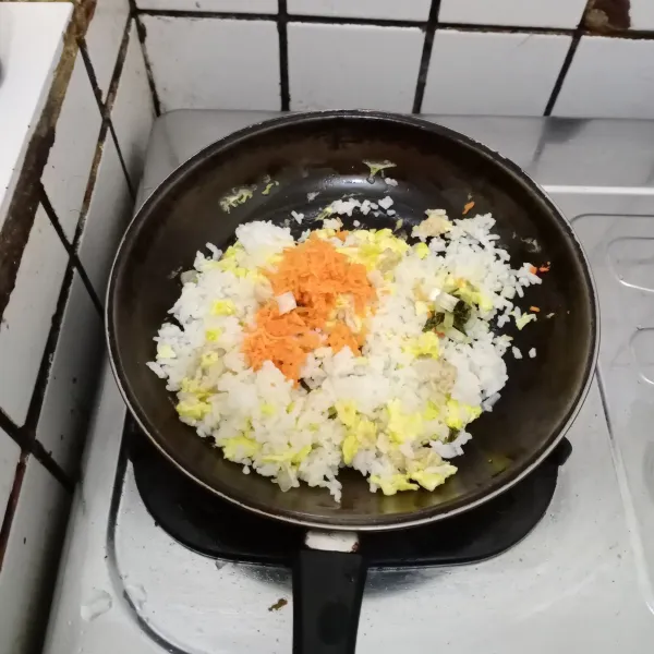 Masukkan nasi, daun bawang dan wortel. 
Aduk rata, masak hingga wortel layu.