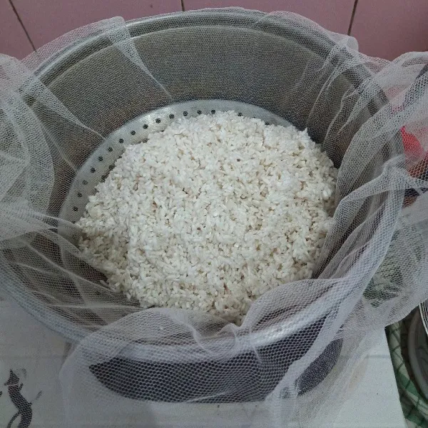 Kukus beras ketan selama 30 menit, kemudian keluarkan beras dari kukusan, pindahkan ke wadah, tambahkan 1 gelas air, aduk rata.