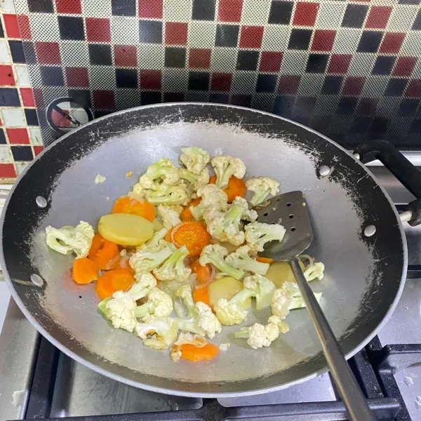 Masukkan irisan kentang, wortel, dan bunga kol, kemudian aduk-aduk hingga sedikit layu.