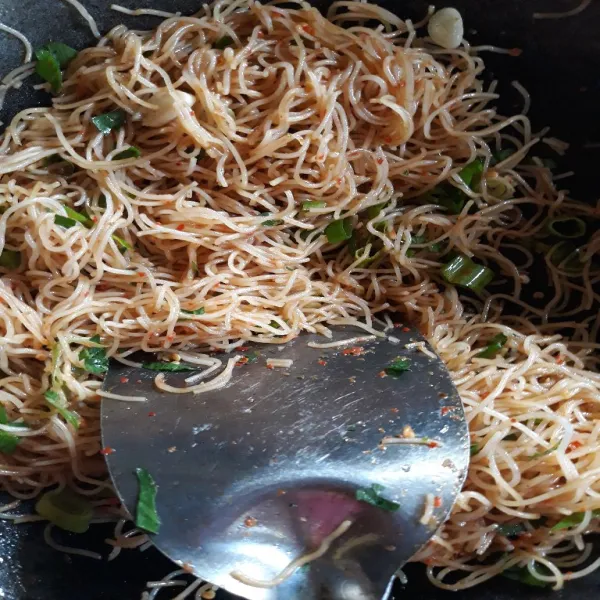 Taburkan daun bawang dan seledri. Nyalakan lagi api kompor dan aduk hingga mihun mengering dan semua bumbu tercampur rata.