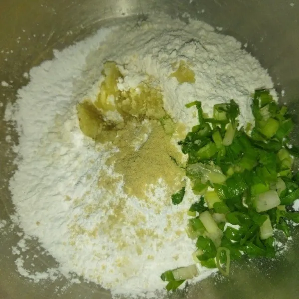 Siapkan wadah, masukkan tepung sagu, tepung terigu, bawang putih halus, garam, kaldu bubuk, dan daun bawang, lalu aduk rata.