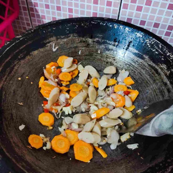 Masukkan wortel dan sosis, kemudian tumis dan aduk rata. Masak hingga wortel layu.