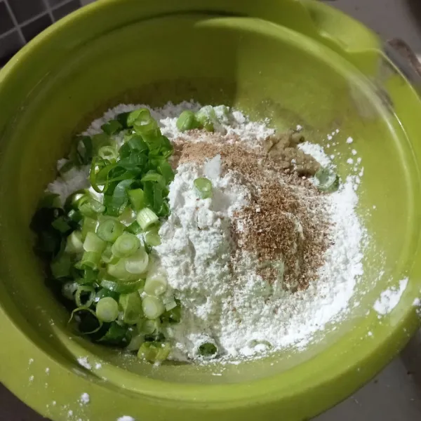 Campur tepung terigu, tepung beras, irisan daun bawang, garam, ketumbar bubuk, kaldu bubuk dan bawang putih halus ke dalam wadah.