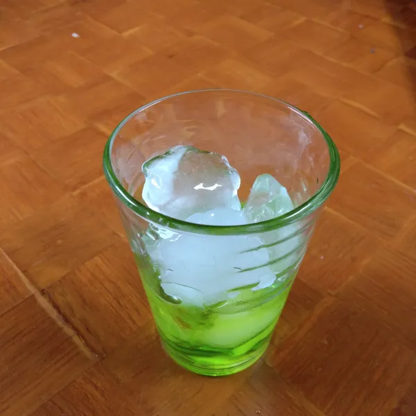 Tuang sirup melon ke dalam gelas. Tambahkan es batu hingga ¾ gelas.