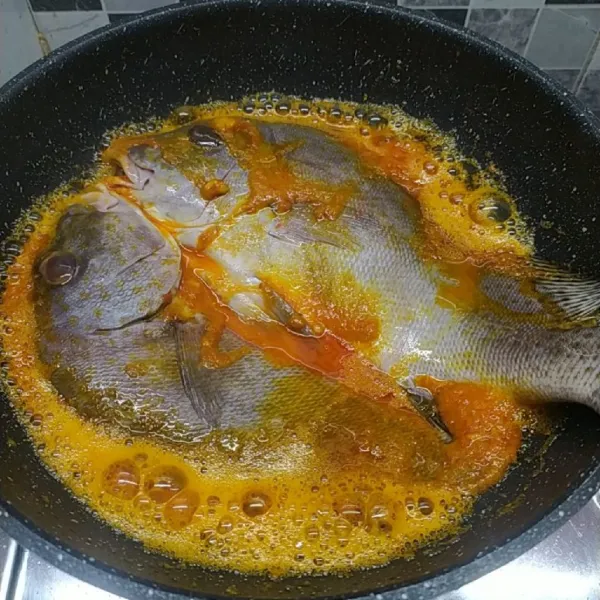 Masukkan ikan perlahan, masak sampai bagian sisi bawah matang sambil bumbu disiram-siram di bagian atas ikan.