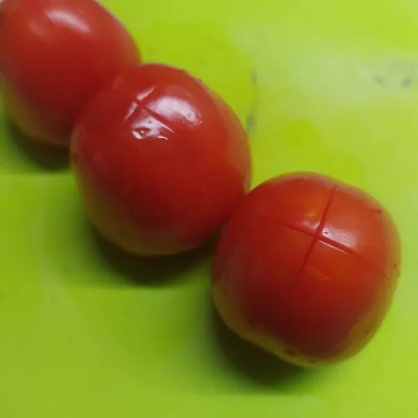 Cuci bersih tomat, lalu kerat bagian atas tomat dengan pisau seperti foto. Ini untuk memudahkan kita saat mengupas kulit tomat.