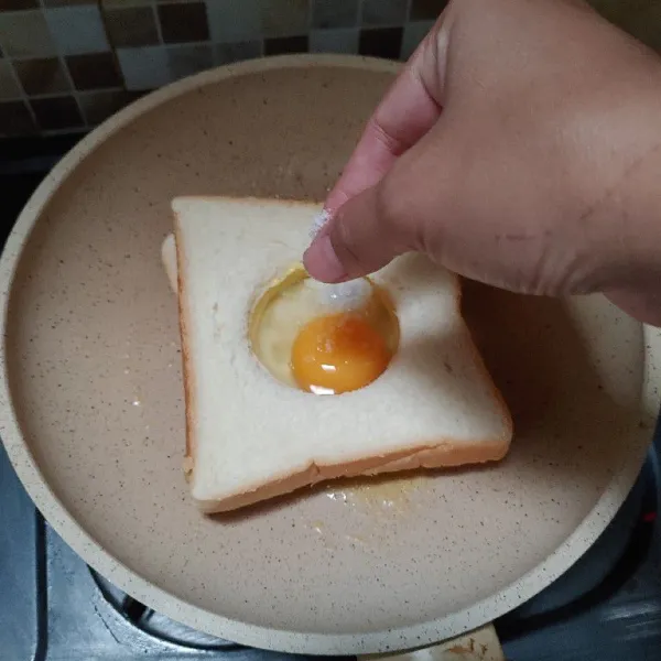 Masukan roti dan isi lubangnya dengan telur, bumbui dengan garam.