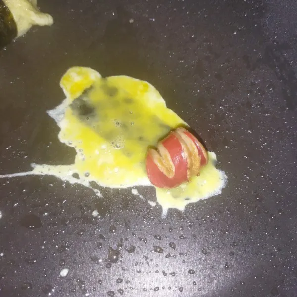 Lalu tuang telur dengan menggunakan sendok makan, lalu taruh sosis di salah satu ujungnya.