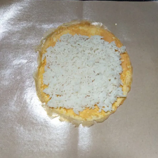 Letakkan telur di atas kertas minyak, setelah itu letakkan nasi di atasnya dan tipiskan.