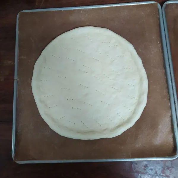 Pipihkan dengan rolling pin, pindahkan ke loyang yang sudah dioles margarin atau pakai alas baking paper. Pipihkan lagi dengan tangan sampai berbentuk bulat dan rapikan. Tusuk-tusuk dengan garpu.
