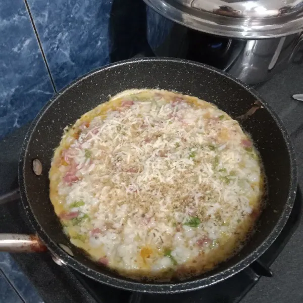 Panaskan teflon dengan margarin, kemudian tuang adonan pizza nasi ke atas teflon. Taburi dengan keju parut dan parsley. Masak dengan api kecil dan tutup teflonnya. Masak hingga sisi bawah berwarna kecokelatan.