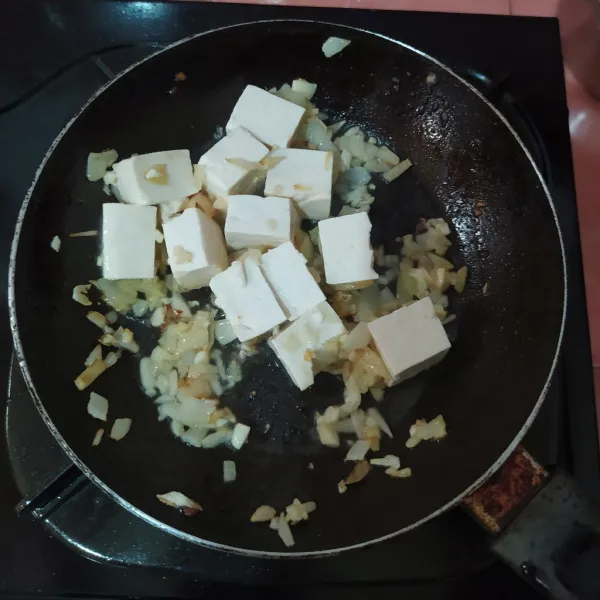 Masukkan minyak wijen, bawang bombay dan bawang putih, tumis hingga harum, lalu masukkan tahu.