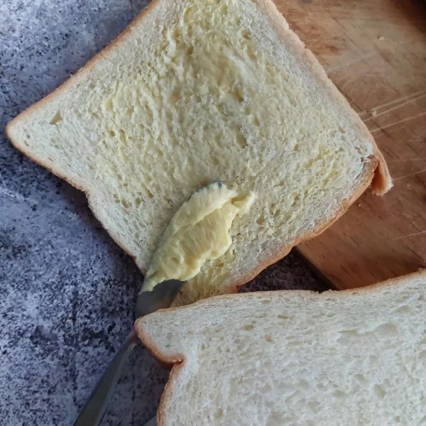 Olesi salah satu permukaan roti dengan margarine.