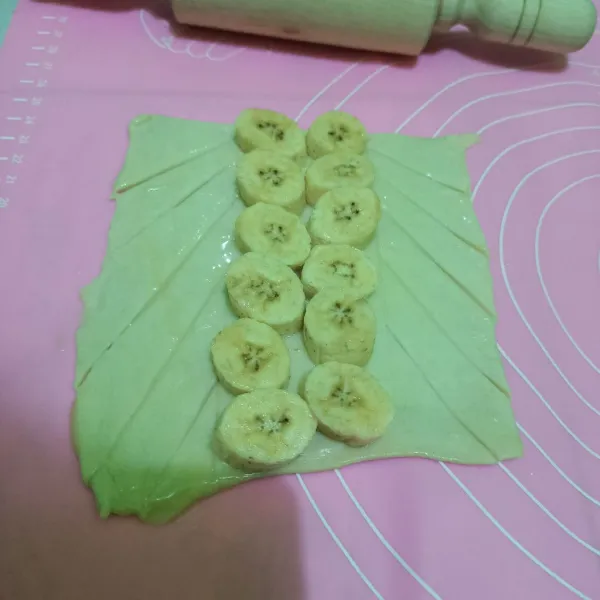 Letakkan pisang tambahkan meses dan keju di tengah kemudian kepang puff pastry. Olesi dengan kuning telur. Lalu beri taburan keju dan meses.